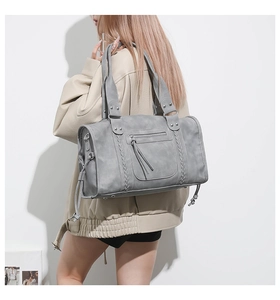 Detailed view of gray vintage leather travel bag with woven texture and long tassels