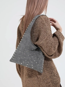 Sac sous le bras en daim gris avec clous argentés porté sur un pull en maille marron