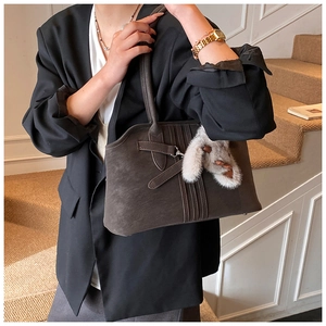Detail of dark brown suede tote bag with vertical stitching and plush bunny charm accessory