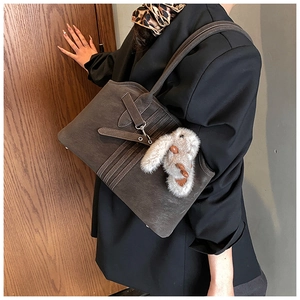 Detail of taupe suede tote bag featuring decorative straps and a plush rabbit pendant