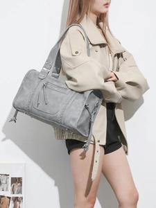 Grey matte travel handbag with woven details and tassel shown on a shoulder