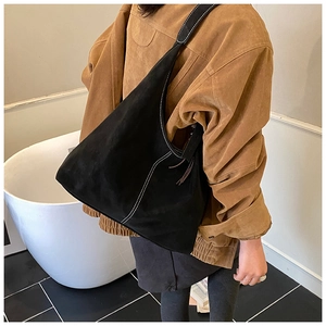 Detail of black matte tote bag with contrast stitching and tassel on a female model