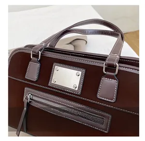 Detail of dark brown tote bag showing silver metal plate and smooth leather handles