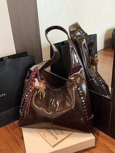 Large dark brown shiny tote bag with silver studs and a bear charm on a wooden table