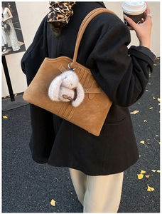 Detail of brown suede tote bag with leather straps and a white bunny plush charm