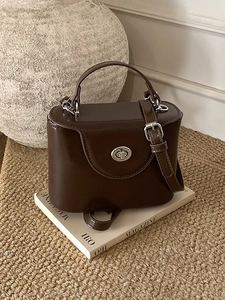 Sac boîte en cuir mat marron foncé avec fermoir rotatif argenté sur fond minimaliste