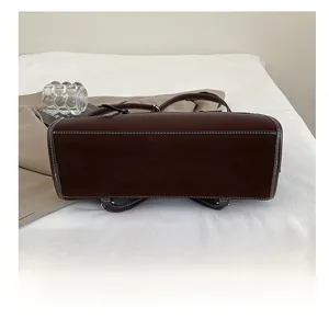 Detail view of durable bag base with white contrast stitching on brown matte leather