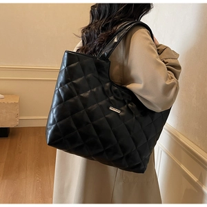 Détail du sac cabas matelassé noir avec plaque logo métallique et texture de cuir