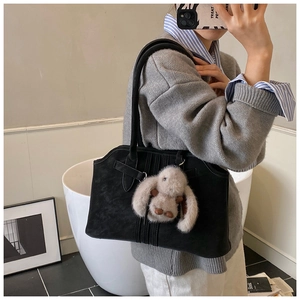 Detail of a black suede tote bag featuring a cute light brown plush rabbit charm