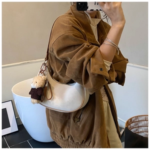 Close-up of white leather crescent hobo bag featuring a cute plush bear pendant accessory