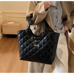 Détail d'un sac cabas noir matelassé avec surpiqûres losanges et plaque dorée