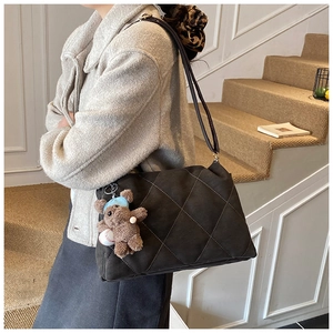 Quilted gray shoulder bag with bear pendant shown on model in warm indoor setting