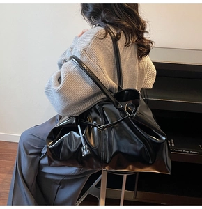On-body view of large black tote bag featuring high-gloss leather and slender shoulder straps