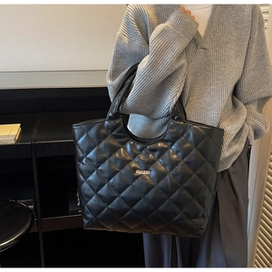 Détail du grand sac cabas noir matelassé avec plaque de logo argentée et texture chic