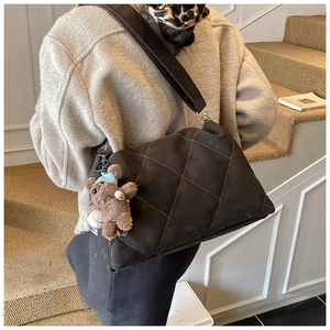 Detail of a large coffee quilted bag with a plush bear charm on a wide fabric strap