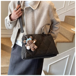 Detail of dark grey quilted crossbody bag with cute plush bear charm on a beige coat