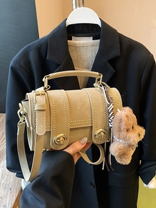 Borsa Boston beige con borchie dorate e ciondolo orsetto davanti a un blazer nero