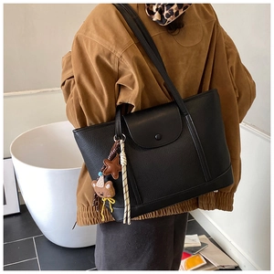 Lifestyle shot of black leather tote bag with plush bear charm on female model