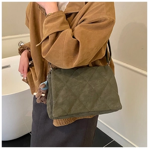 Detail of dark green quilted shoulder bag with a brown knit bear charm accessory