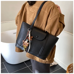 Detail of black pebbled leather tote bag with stylish bear plush charm and snap closure