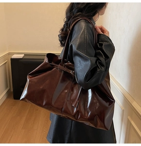Close-up of a large brown glossy PU leather tote bag with stylish side strap details