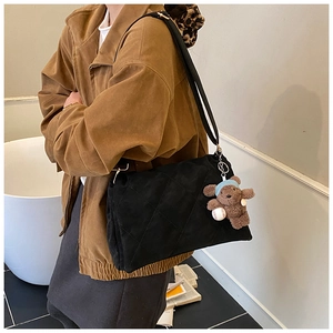 Detail of black quilted shoulder bag featuring a cute brown plush bear charm and textured fabric