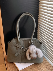 Vintage olive green suede tote bag with plush bunny pendant on a wooden surface