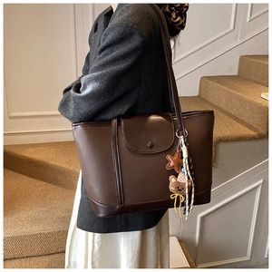 Detail of dark brown pebble leather tote bag with bear charm on grey suit model