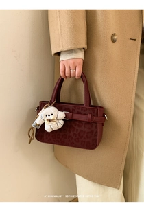 Détail d'un sac en cuir bordeaux avec motif léopard et un pendentif ours en peluche