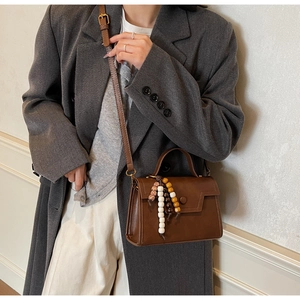 Détail d'un sac bandoulière vintage marron avec pendentif perlé et sangle réglable