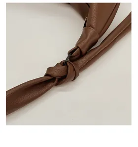 Detail of adjustable knotted wide leather strap with dark metal buckle on brown tote bag