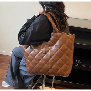 Détail d'un grand sac cabas matelassé marron montrant son logo métallique élégant