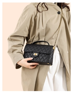 Close-up of black quilted leather bag featuring a gold lock and chain strap detail