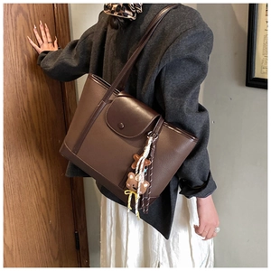 Detail of dark brown tote bag with lychee texture and cute bear tassel charm