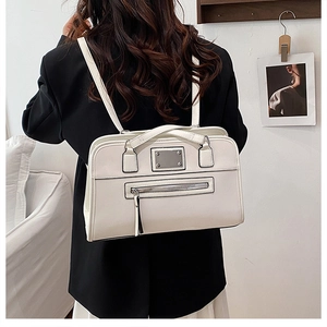 Detailed view of white leather tote bag with metallic logo and fringe zipper on black blazer
