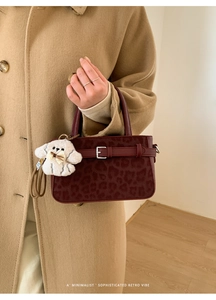 Détail du sac à main bordeaux imprimé léopard avec peluche tenu par un mannequin