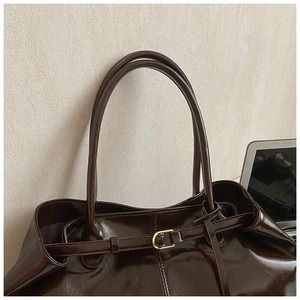 Detail of dark brown tote bag handle with shiny finish and gold buckle accent