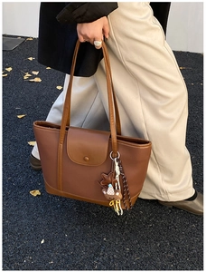 Detail of caramel leather tote bag with pebble texture and cute bear charm in autumn setting