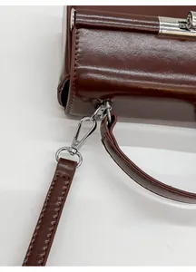 Detail view of the high-shine brown leather bag featuring a detachable thin shoulder strap