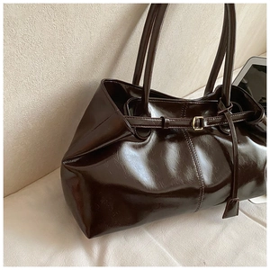 Detail of dark brown tote bag showing glossy leather texture and gold metal buckle
