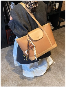 Detail view of camel lychee leather tote bag with star and bear charms on shoulder