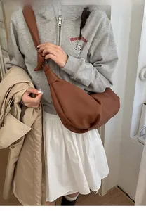 Detail of a brown leather crescent bag featuring a unique knotted strap design on a model