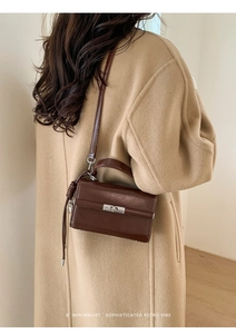 Detail of dark brown retro leather handbag styled with a camel wool coat in soft indoor light