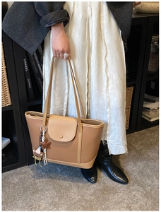 Close-up of brown faux leather tote bag featuring a star and bear bag charm and top handles