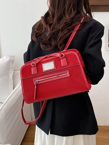 Retro red faux leather tote bag with silver plate detail worn on shoulder with black blazer