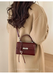 Deep red patent leather bag detail with silver lock and tassel shown on a camel coat
