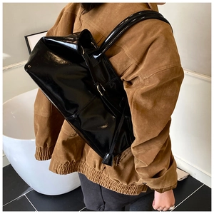 Detail of black glossy patent leather tote bag with metallic adjustable buckle on shoulder strap
