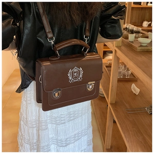 Retro brown leather crossbody bag with shield embroidery shown in a lifestyle setting