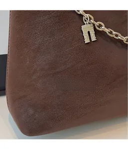 Detail of dark brown leather tote with silver chain and iconic metal charm