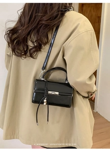 Detail of black patent leather square bag with metallic buckle and elegant tassel charm